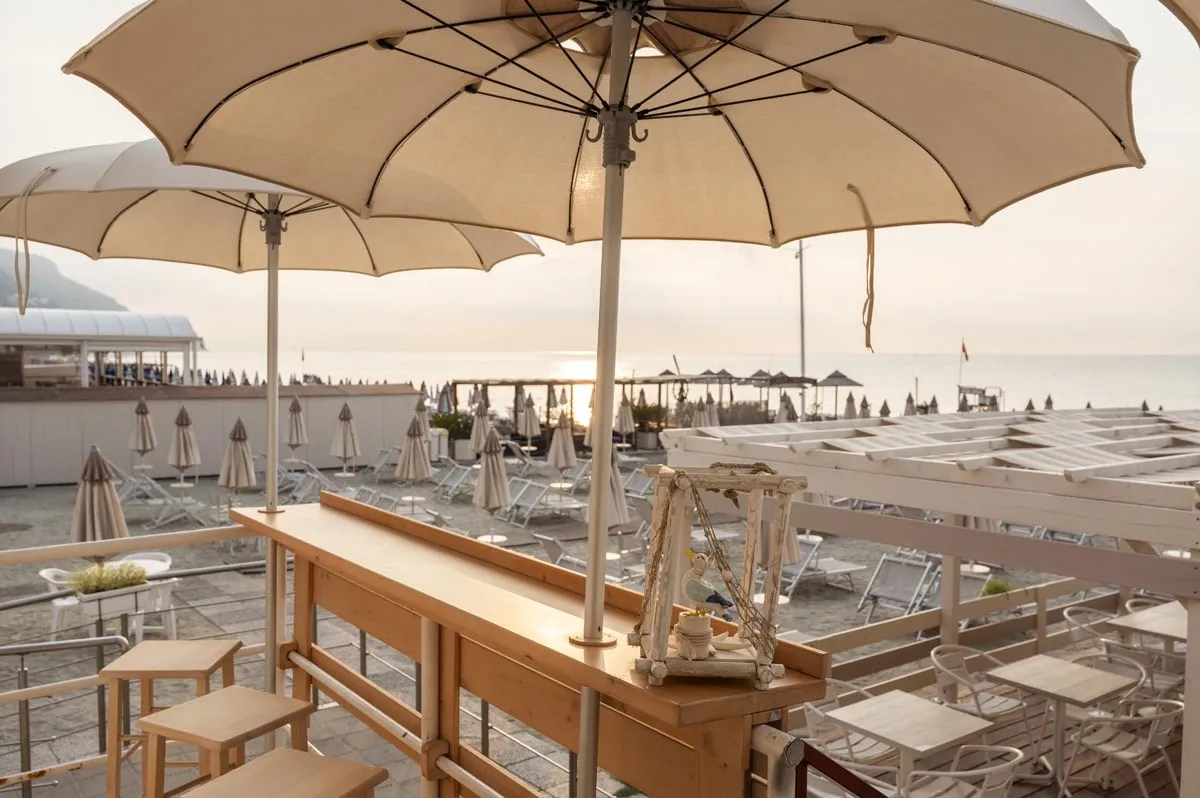 Terrazza bar sulla spiaggia con ombrelloni e vista sul mare al tramonto