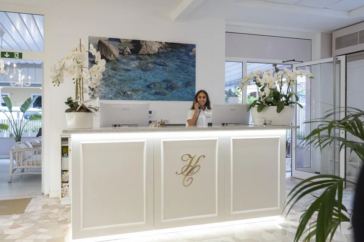 Reception dell'hotel con bancone bianco, orchidee e addetta al lavoro