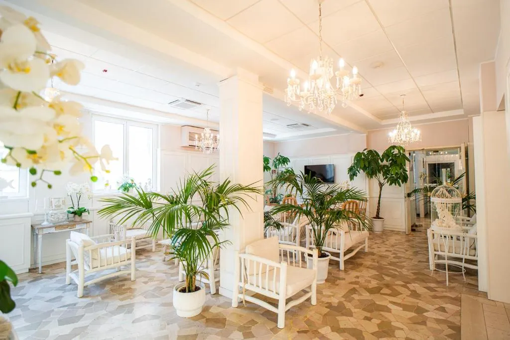 Hall luminosa con poltrone bianche, piante verdi e lampadari di cristallo
