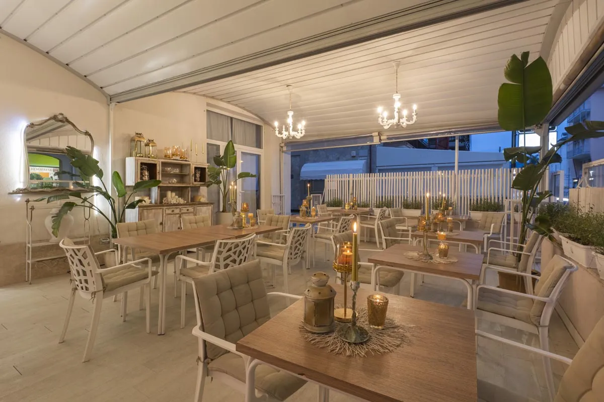 Sala ristorante veranda con tavoli in legno, candele e atmosfera serale