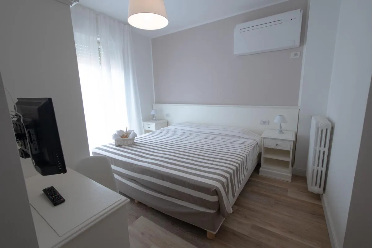 Camera con letto matrimoniale a righe, TV e pavimento in legno