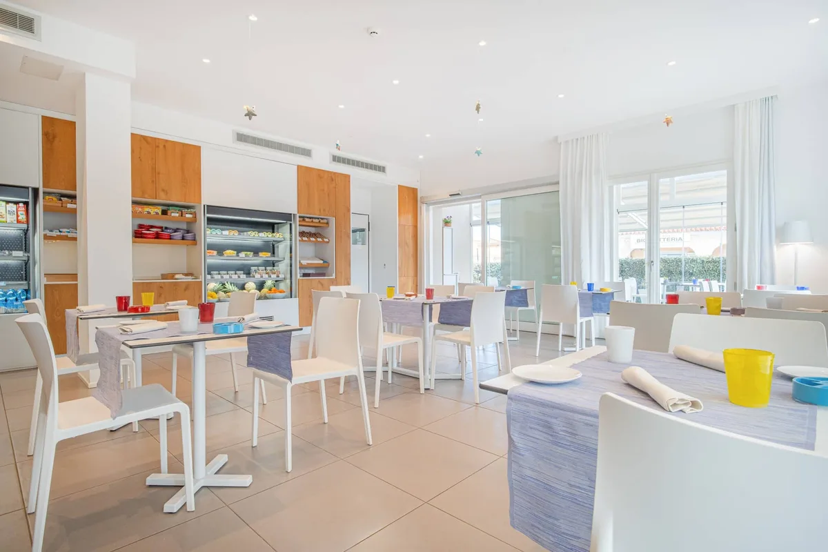 Sala colazione luminosa con tavoli bianchi e buffet
