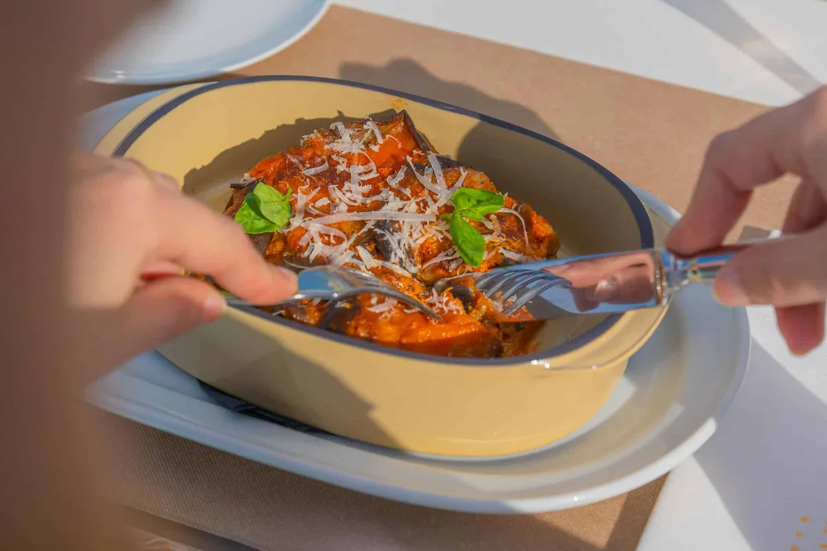 Parmigiana di melanzane servita in pirofila con basilico
