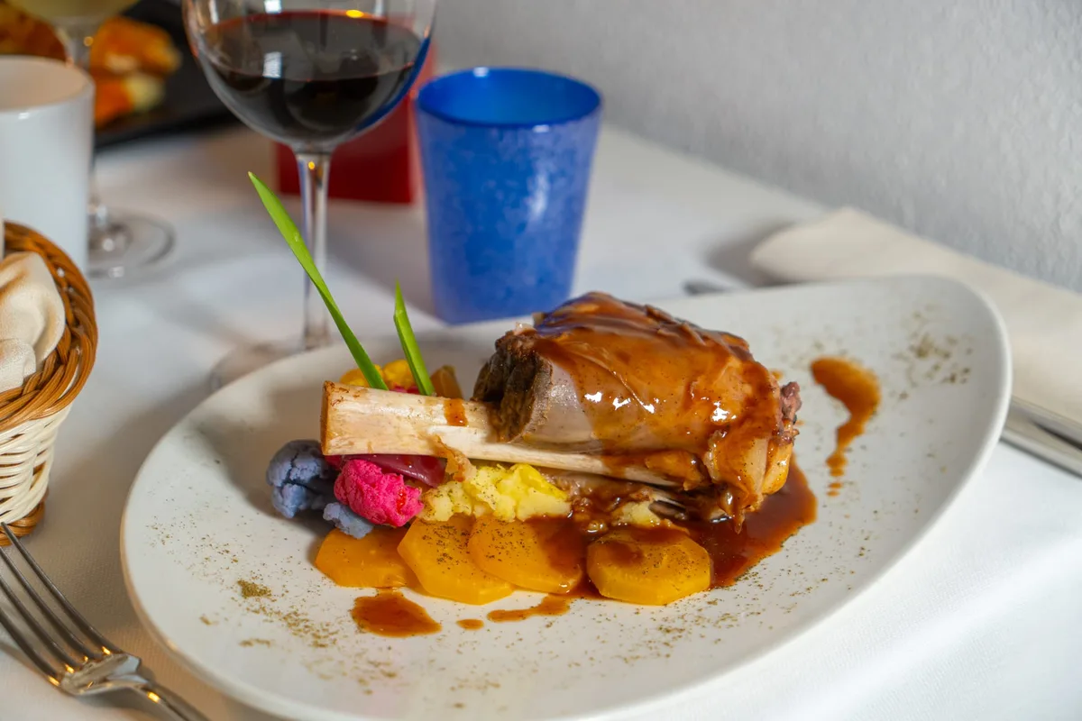 Stinco di maiale glassato con purè e verdure e calice di vino rosso