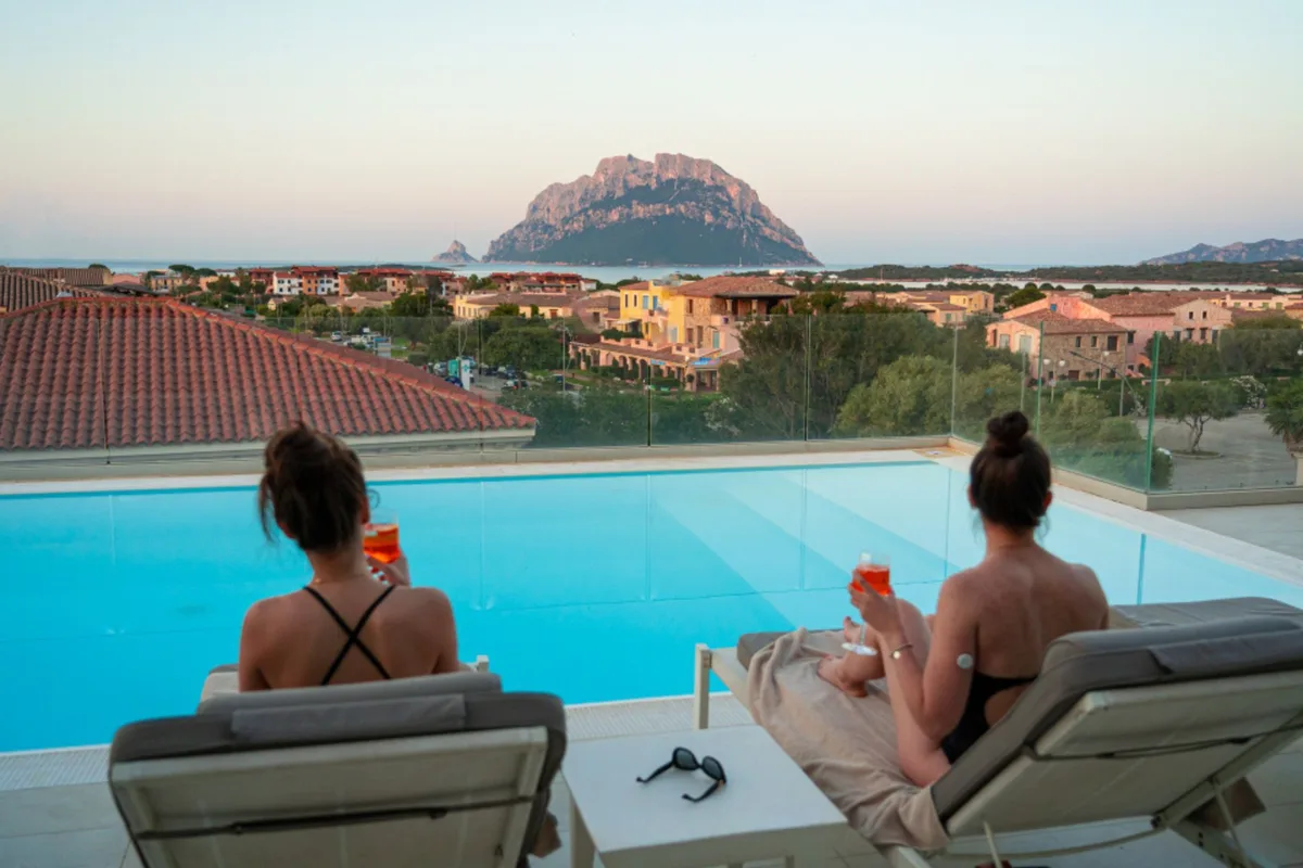 Due donne rilassate sui lettini con aperitivo e vista sull'Isola di Tavolara al tramonto