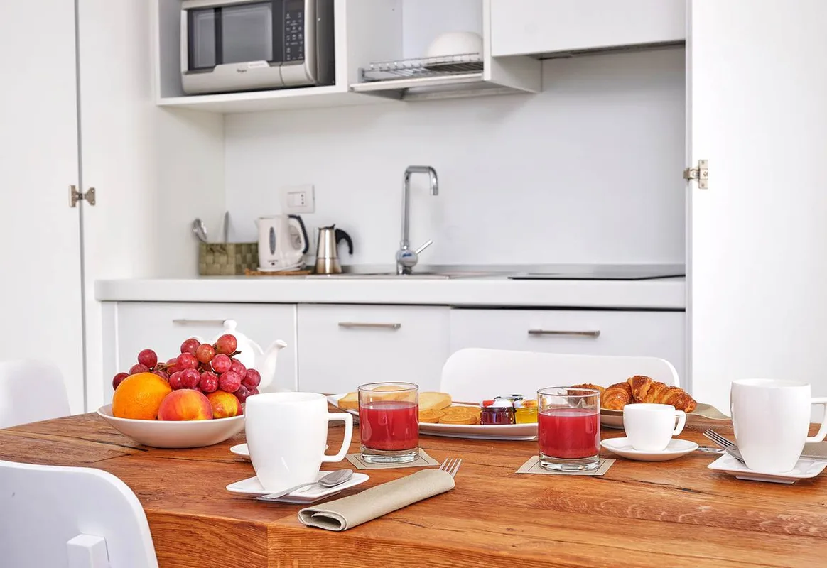 Tavolo per la colazione con frutta, succhi e cornetti davanti all'angolo cottura