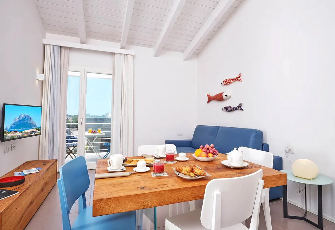 Soggiorno con tavolo da pranzo apparecchiato, divano blu e balcone vista mare