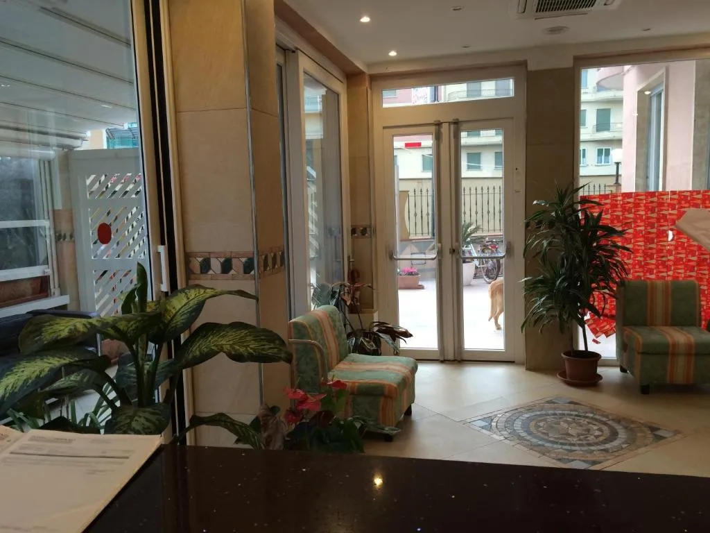 Area lobby con poltrone, piante e ingresso vetrato verso la strada