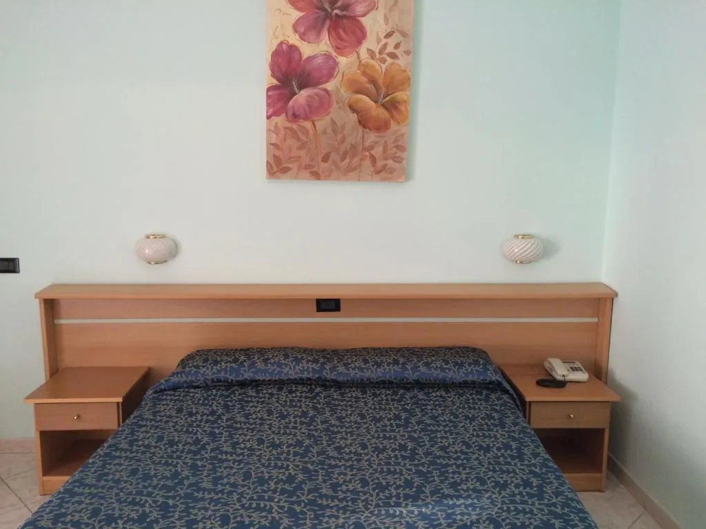 Letto matrimoniale con testiera in legno, comodini e decorazione floreale alla parete