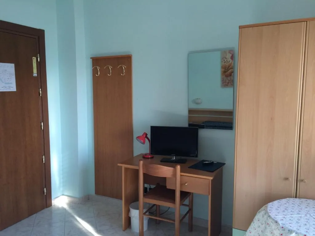 Camera con scrivania, sedia, televisore, armadio e specchio