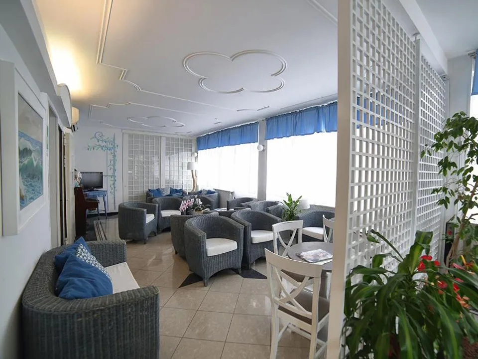 Salotto dell'hotel con poltrone in vimini, divani e ampie finestre con tende blu
