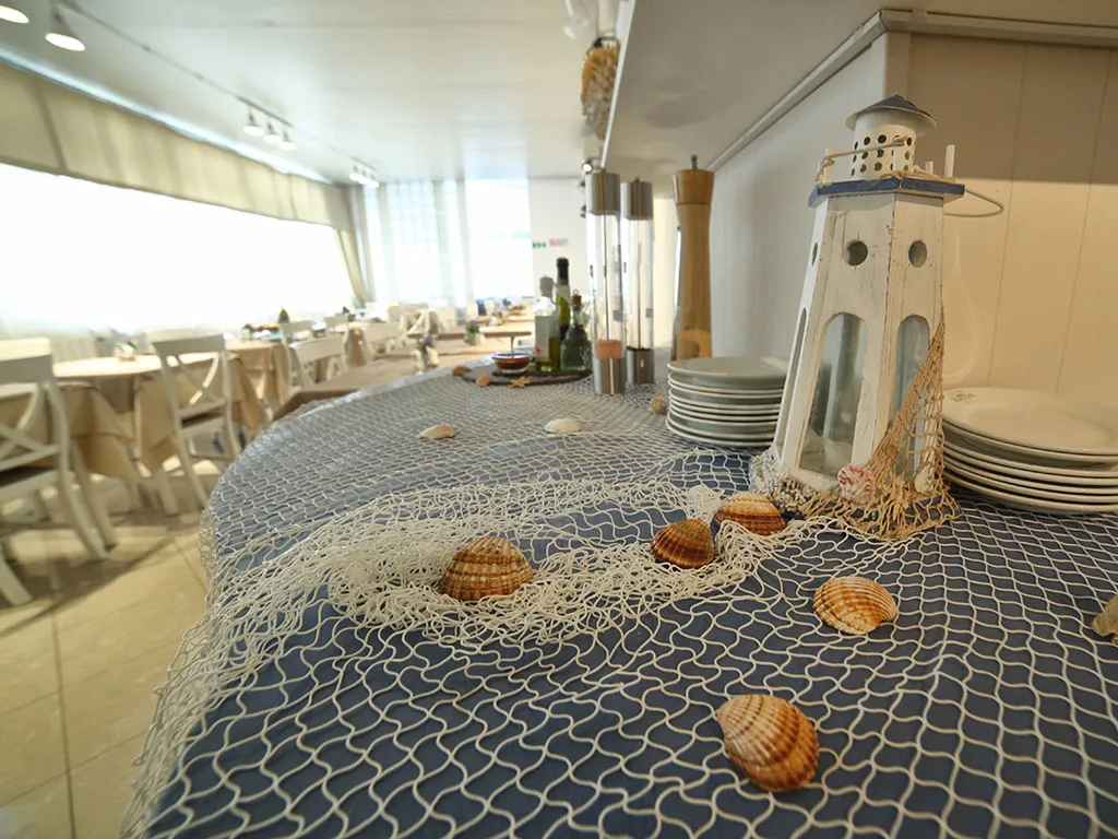 Dettaglio di tavolo decorato con rete da pesca, conchiglie e lanterna a forma di faro