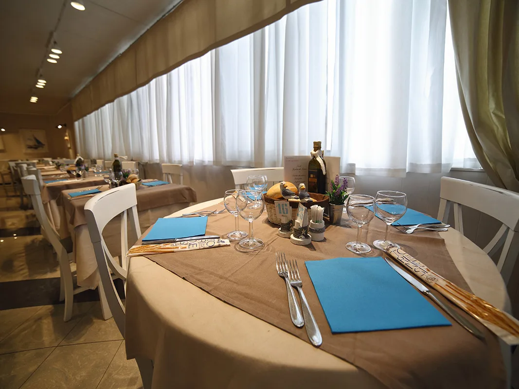 Tavolo del ristorante apparecchiato con tovaglioli azzurri e bicchieri vicino a grandi finestre