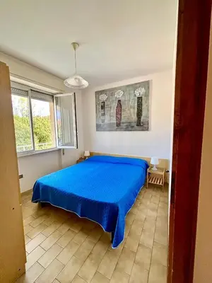 Camera da letto matrimoniale con copriletto blu, finestra e quadro decorativo
