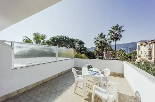 Ampia terrazza con tavolo e sedie bianche, vista su palme, montagne e giardino