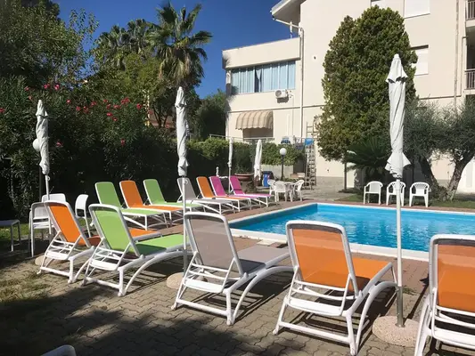 Lettini colorati arancioni, verdi e rosa accanto alla piscina in un giardino con palme