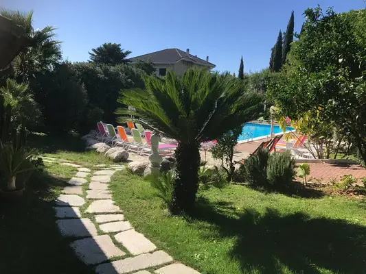 Giardino con vialetto in pietra, palme e piscina con lettini colorati sullo sfondo