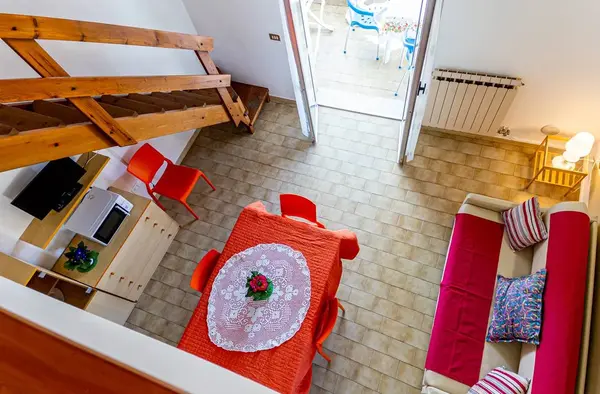 Vista dall'alto di appartamento su due livelli con scala in legno, tavolo e divano
