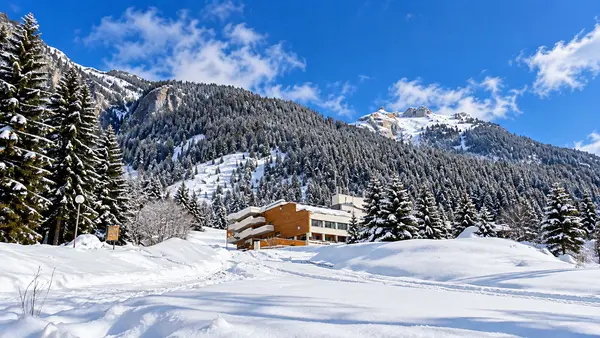 Hotel di montagna immerso nella neve con pinete e vette innevate sullo sfondo