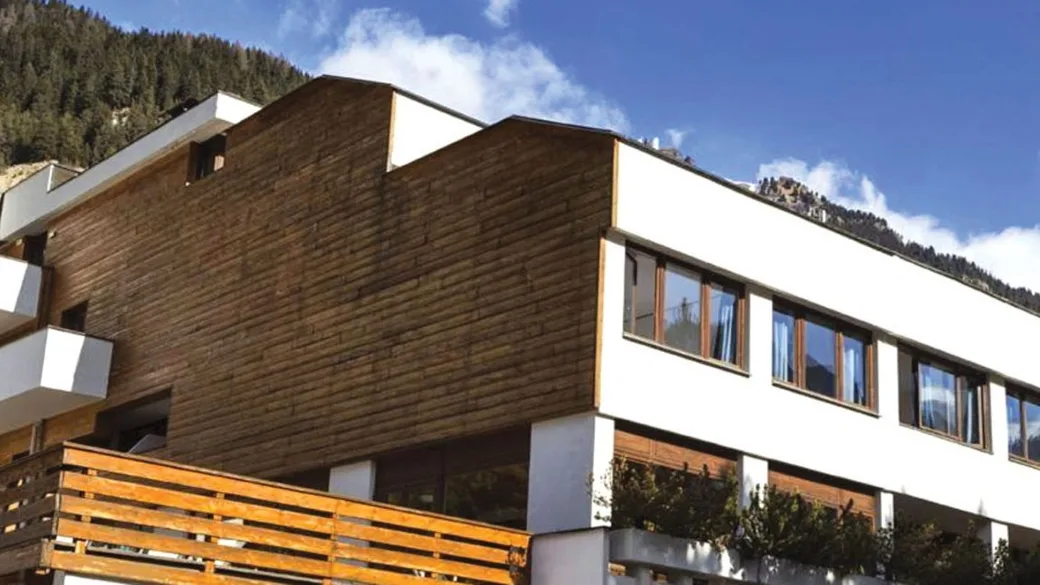 Facciata esterna dell'hotel con rivestimenti in legno e pareti bianche sullo sfondo di montagne boscose