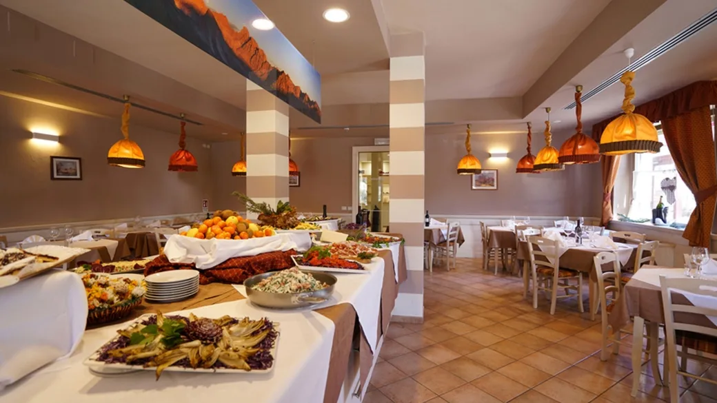 Sala ristorante con buffet ricco di piatti e tavoli apparecchiati con lampade arancioni