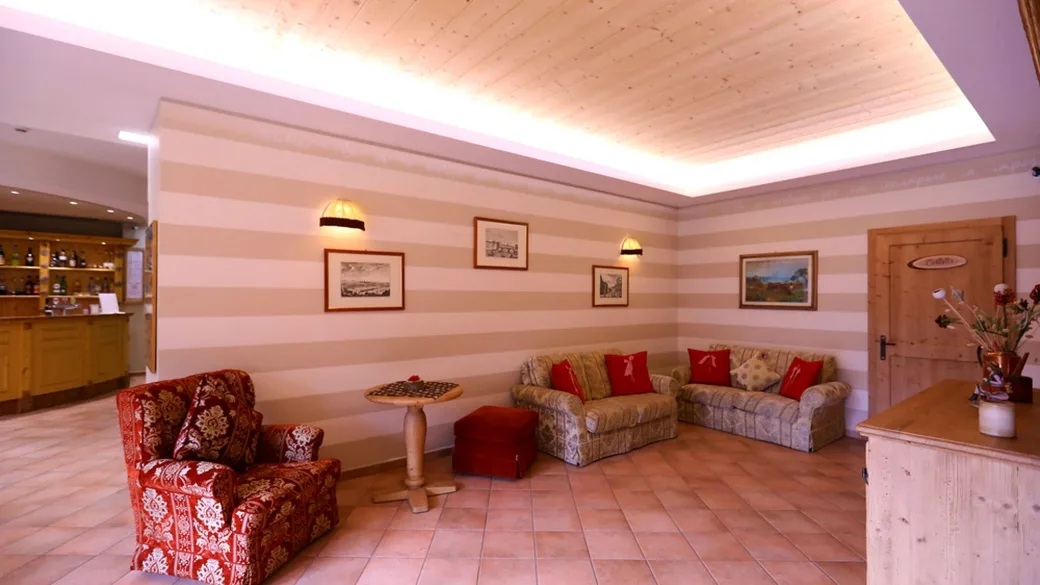Salottino d'ingresso con poltrone, divani e pareti a righe in tonalità calde