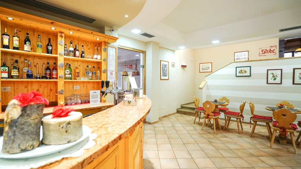 Zona bar con bancone in legno, bottiglie e tavolini in stile tirolese