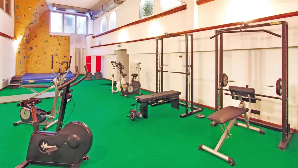 Palestra dell'hotel con attrezzi cardio, pesi e parete da arrampicata su pavimento verde