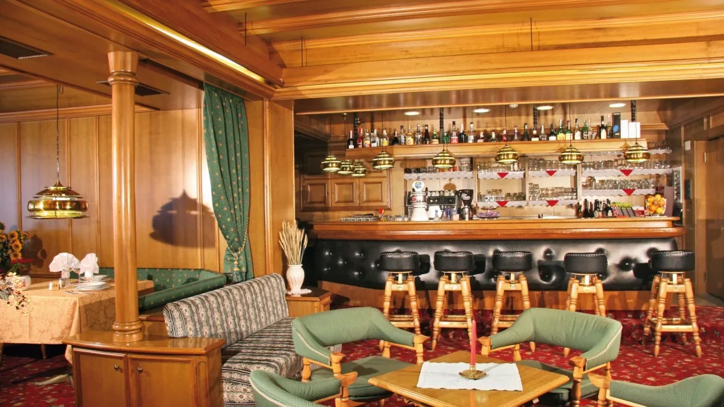 Bar dell'hotel con bancone in legno, sgabelli imbottiti e poltrone verdi in zona lounge