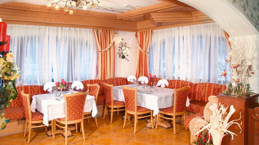 Sala ristorante con tavoli apparecchiati, sedute rosse imbottite e decorazioni floreali