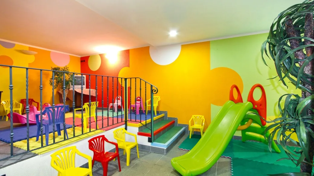 Sala giochi per bambini colorata con scivolo verde, sedie e tappeti morbidi