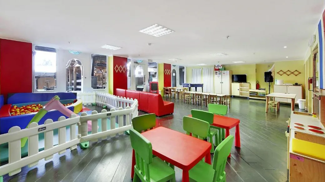Sala giochi per bambini con tavolini colorati, area morbida e mobili a misura di bimbo