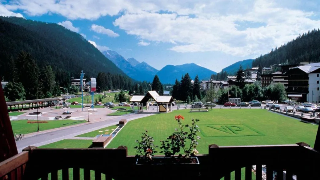 Vista panoramica dal balcone su prato verde, montagne e centro turistico alpino