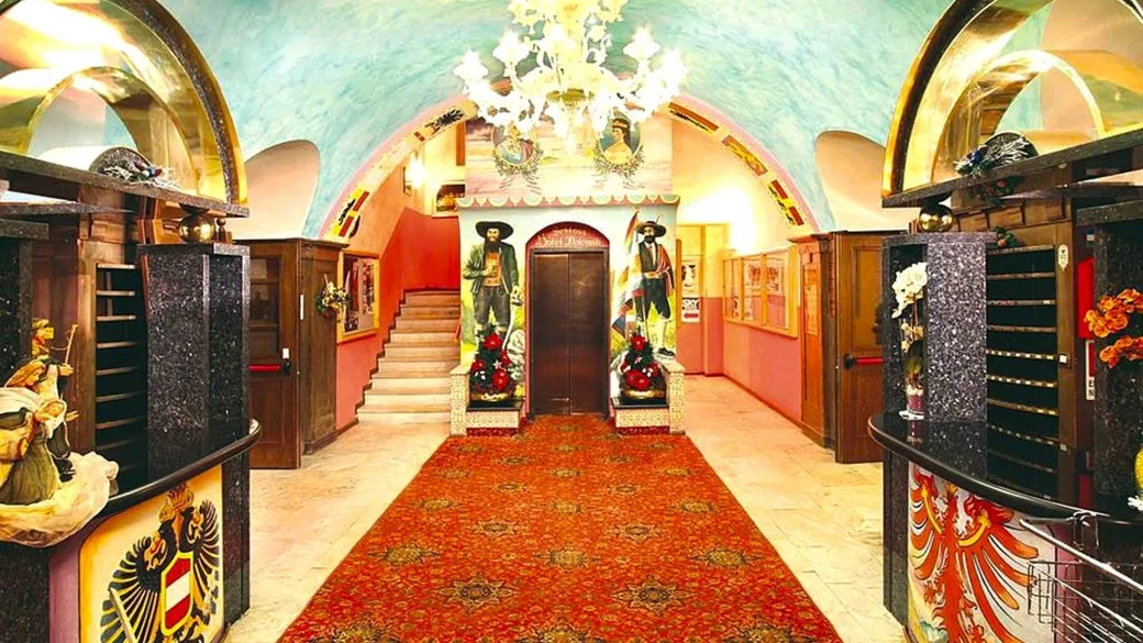 Hall dell'hotel con volte affrescate, lampadario di cristallo, tappeto rosso e reception con stemmi araldici