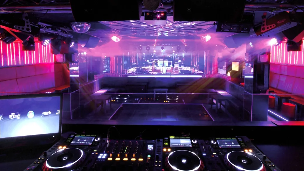 Discoteca con luci al neon rosa e viola, console DJ e palco illuminato