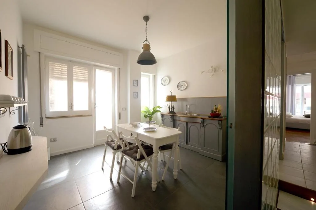 Cucina e zona pranzo con tavolo bianco, sedie, lampada a sospensione e vista sulla camera da letto