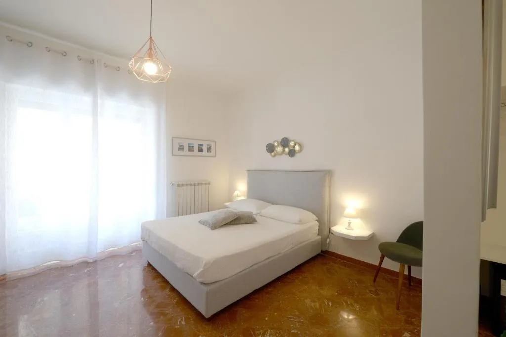 Camera da letto luminosa con letto matrimoniale, testiera grigia, pavimento in marmo e ampia finestra
