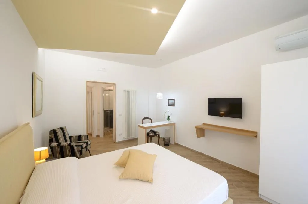 Ampia camera moderna con letto matrimoniale, poltrona a righe, scrivania e TV a parete