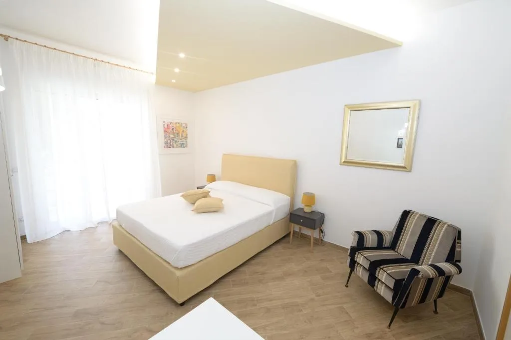 Camera da letto con letto matrimoniale, poltrona a righe, specchio dorato e pavimento in legno