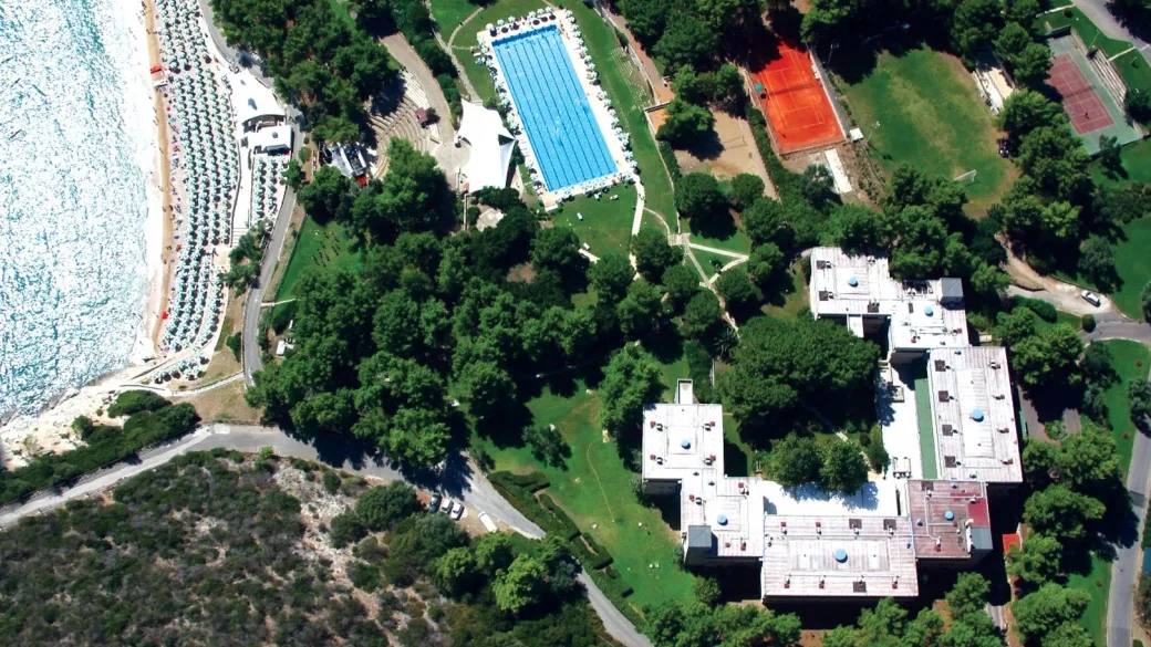 Vista aerea del complesso con grande piscina, campi da tennis, spiaggia e vegetazione