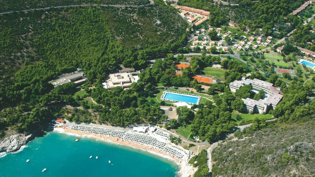 Veduta aerea del villaggio con piscina, campi sportivi, ville immerse nel verde e spiaggia sul mare turchese