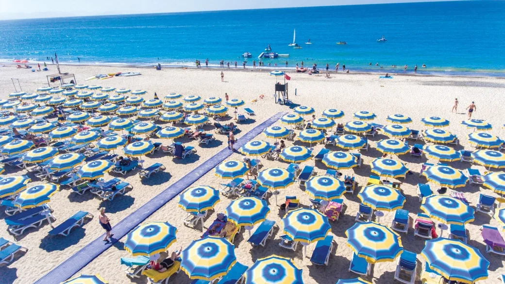 Spiaggia attrezzata con ombrelloni blu e gialli vista dall'alto sul mare