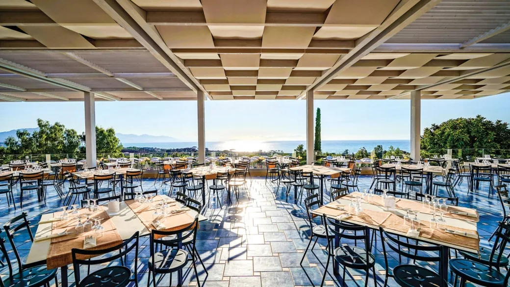 Ristorante con terrazza panoramica e tavoli apparecchiati con vista sul mare al tramonto