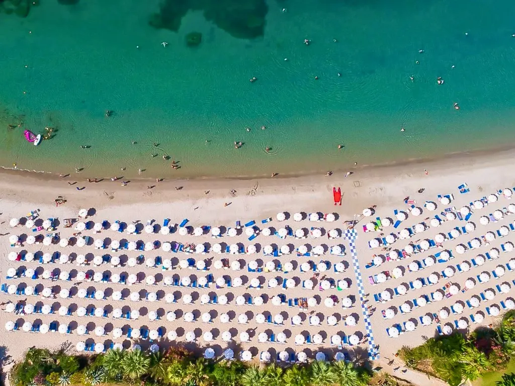Veduta aerea della spiaggia con file di ombrelloni bianchi e mare turchese