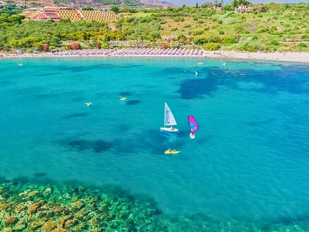 Baia con acque cristalline, barca a vela e windsurf davanti all'hotel