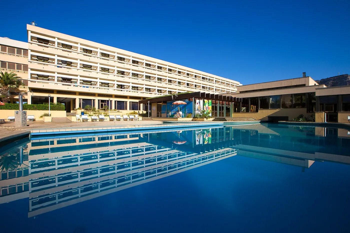 Facciata dell'hotel riflessa nell'ampia piscina esterna con cielo azzurro