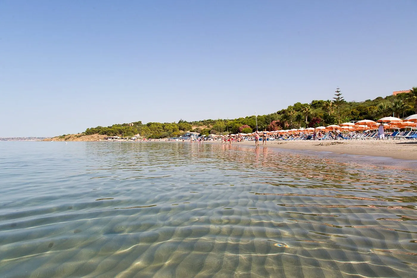 Spiaggia sabbiosa vista dal mare con acque limpide e ombrelloni colorati
