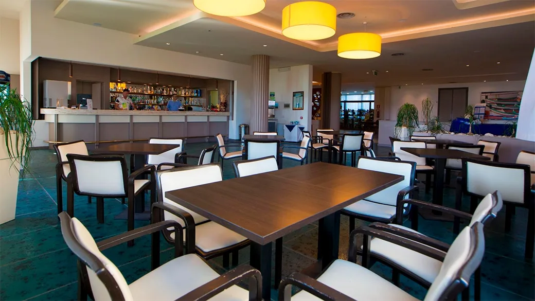 Area bar interna con tavoli, sedie e bancone illuminato