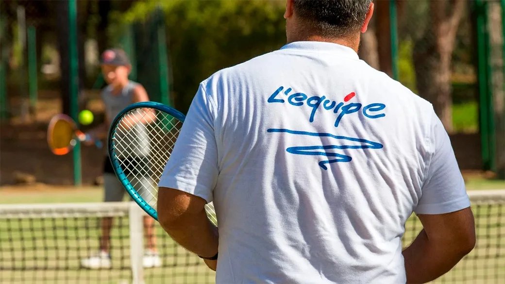 Istruttore di tennis con maglietta L'equipe durante una lezione in campo
