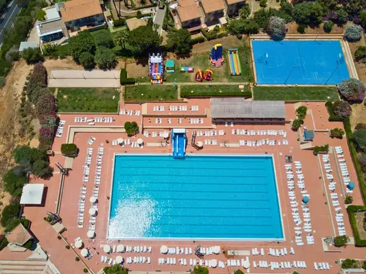 Panoramica aerea della piscina con scivolo, lettini bianchi, gonfiabili e campo da basket